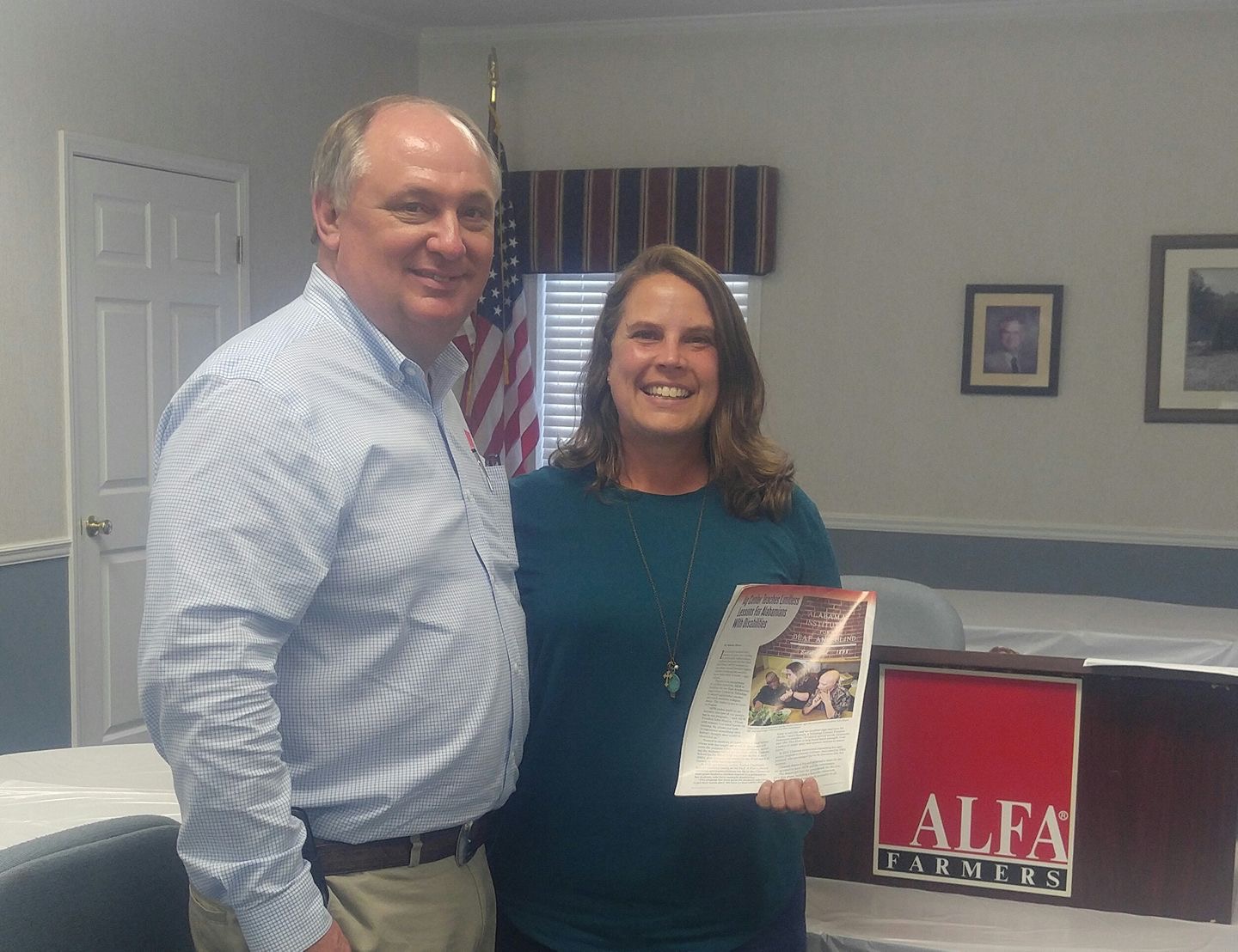 Two people standing in a classroom holding up a picture.  